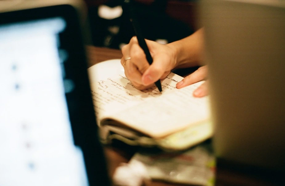 Person writing in notebook near laptop