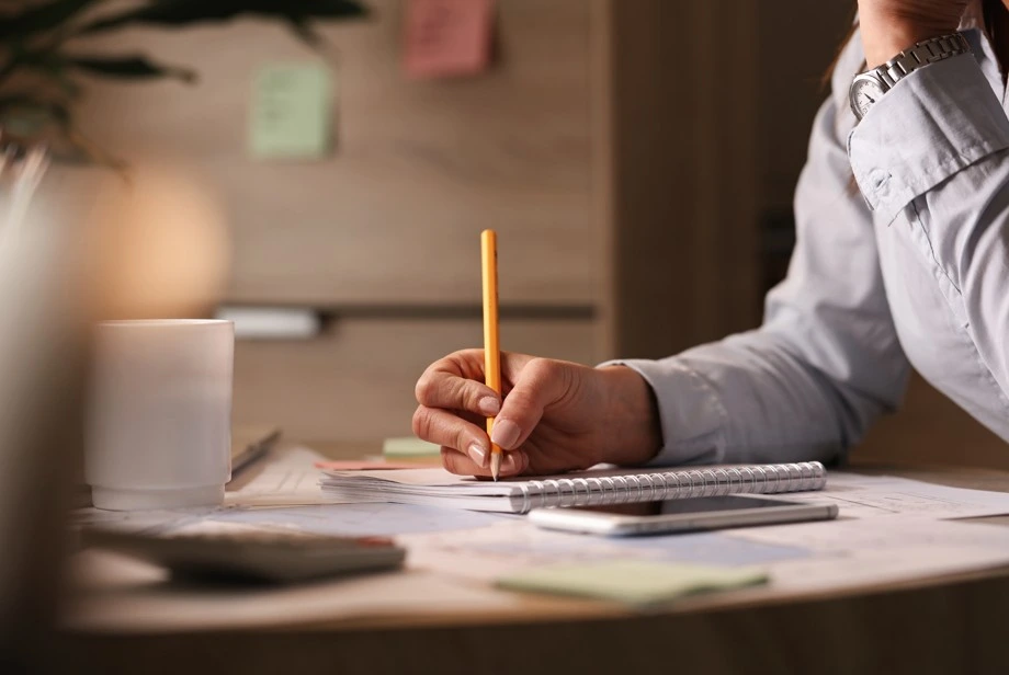 Person writing notes on a desk with pencil and notebook
