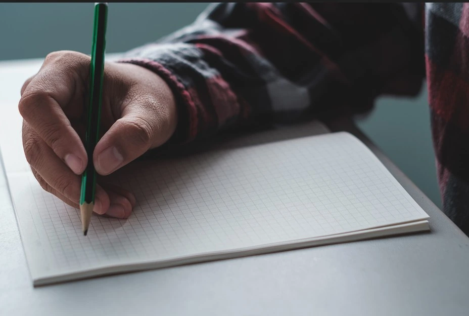 person writing in notebook with pencil