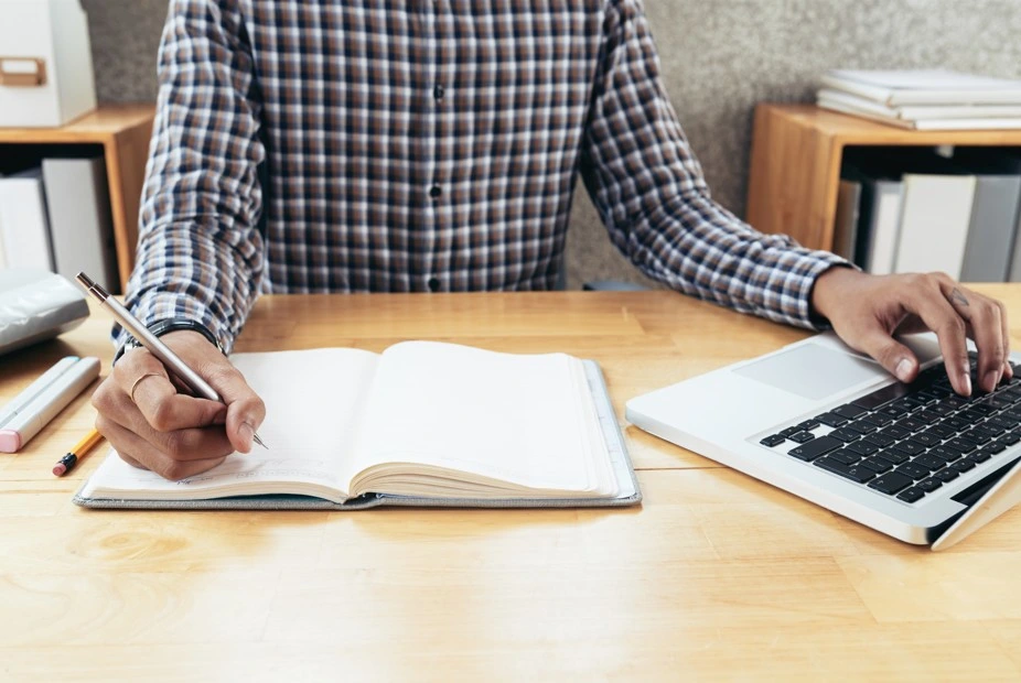 man working on laptop and writing notes